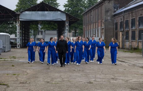 Une chorale en vêtements bleus marche dans un espace industriel.